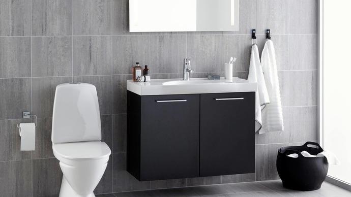 Moderne badeværelse med sort vaskeskab, spejl, toilet og håndklæder på væggen.