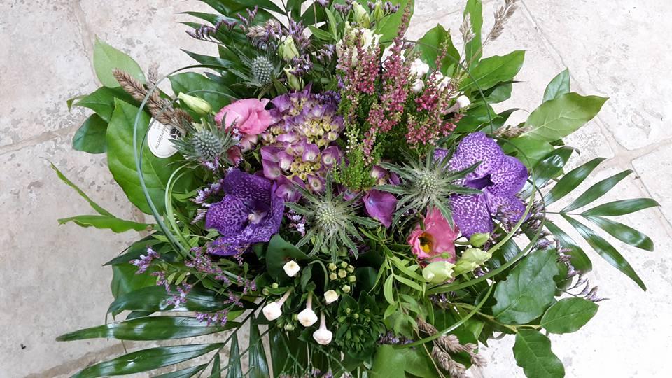 En farverig buket med lilla blomster, grønne blade og forskellige planter i en smuk sammensætning.
