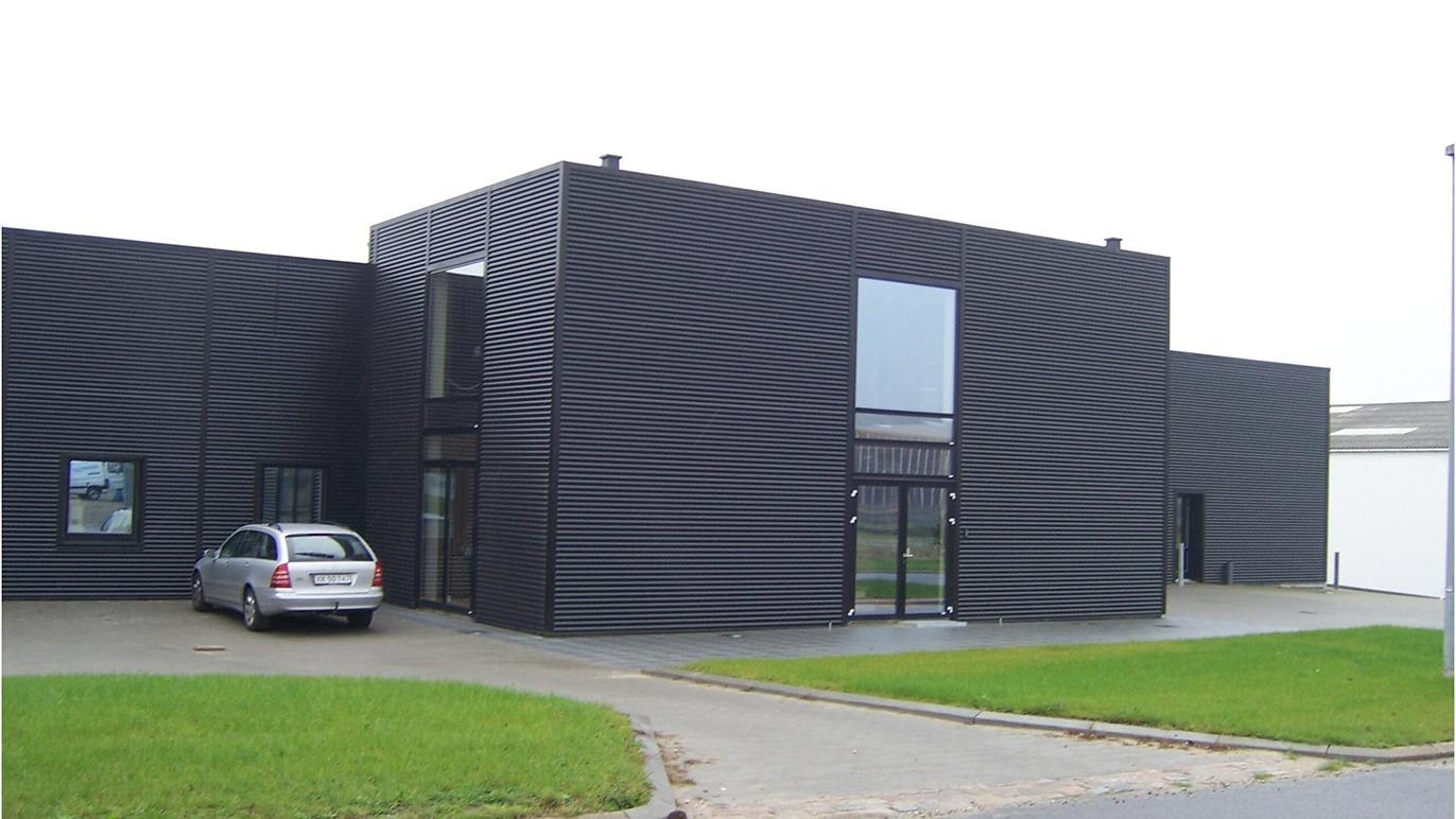 Moderne sort bygning med bølgede vægge og store vinduer, parkeret bil foran indgangen.