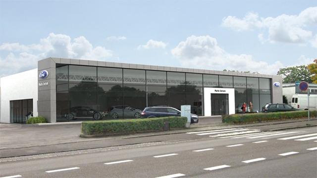 Moderne bilforhandler med store vinduer og biler parkeret foran, beliggende ved en vej.