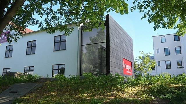 Moderne bygning med glasfacade og grønne omgivelser, beliggende ved en skråning.