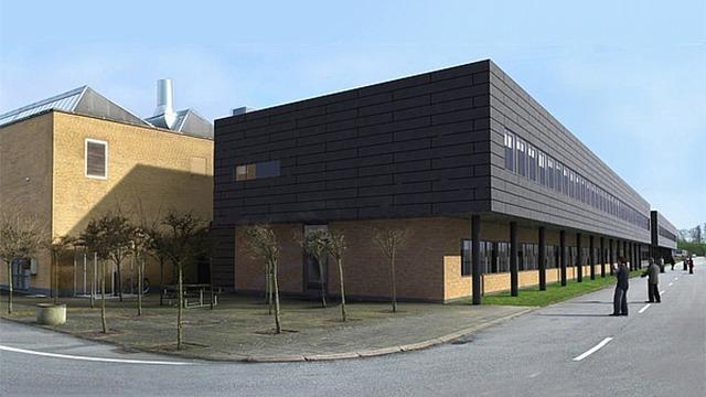 Moderne bygning med sort facade og store vinduer, omgivet af træer og en asfalteret vej.