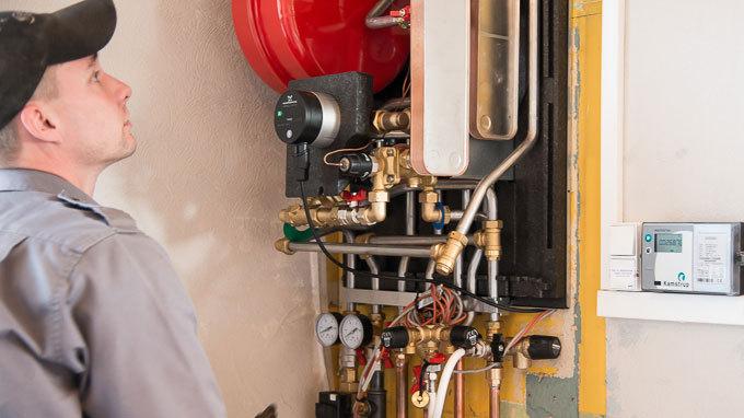 En tekniker inspicerer en varmepumpe med rør og måleinstrumenter i en bolig.