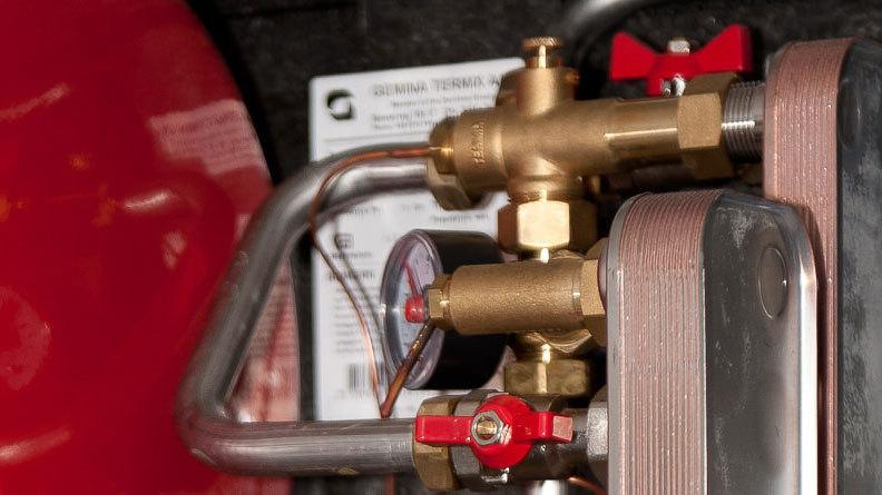 Detalje af en trykregulator med messingventiler og måler i en rød gasbeholder.