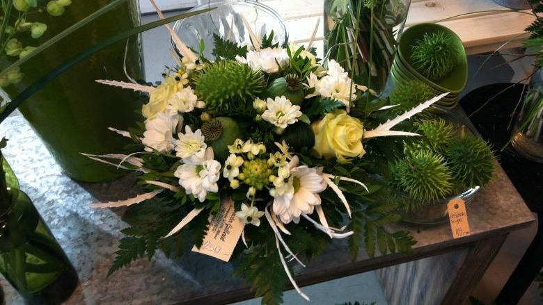 En smuk blomsterbuket med hvide og grønne blomster, prydet med grønne blade og dekorative elementer.