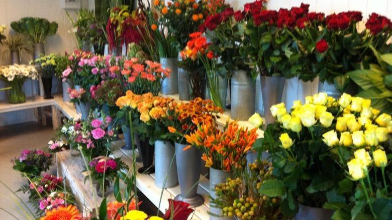 En blomsterbutik med farverige buketter af roser, nelliker, liljer og andre blomster i metalspande.