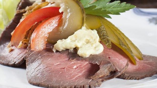 Lækkert stykke roastbeef med syltede grøntsager og sennep på en tallerken.