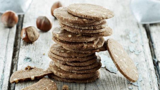 Lækre chokolade småkager stablet på et træbord med hasselnødder i baggrunden.