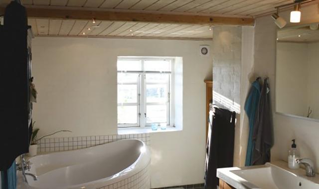 Lyst badeværelse med badekar, håndvask og vindue, der giver naturligt lys.