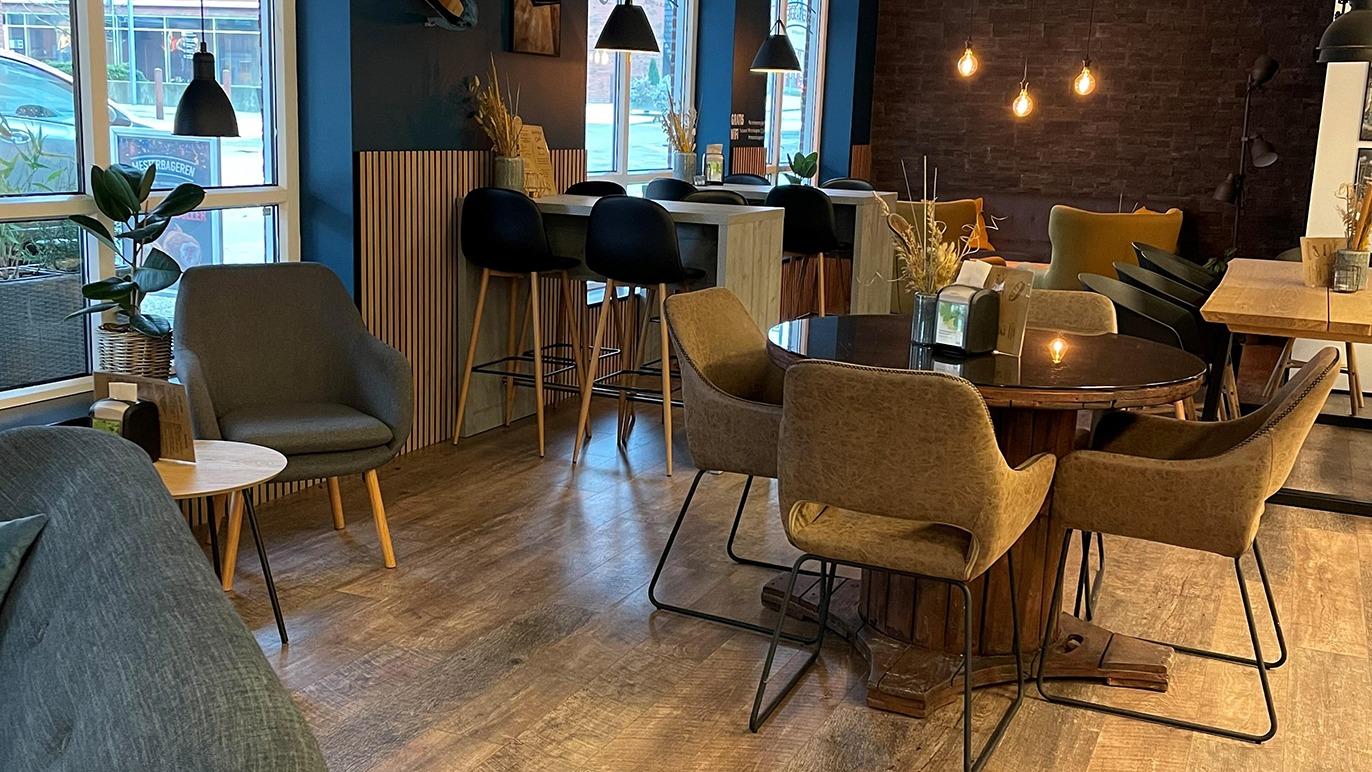 Moderne indretning af en café med borde, stole og barstole i et lyst rum med vinduer og hyggelig belysning.