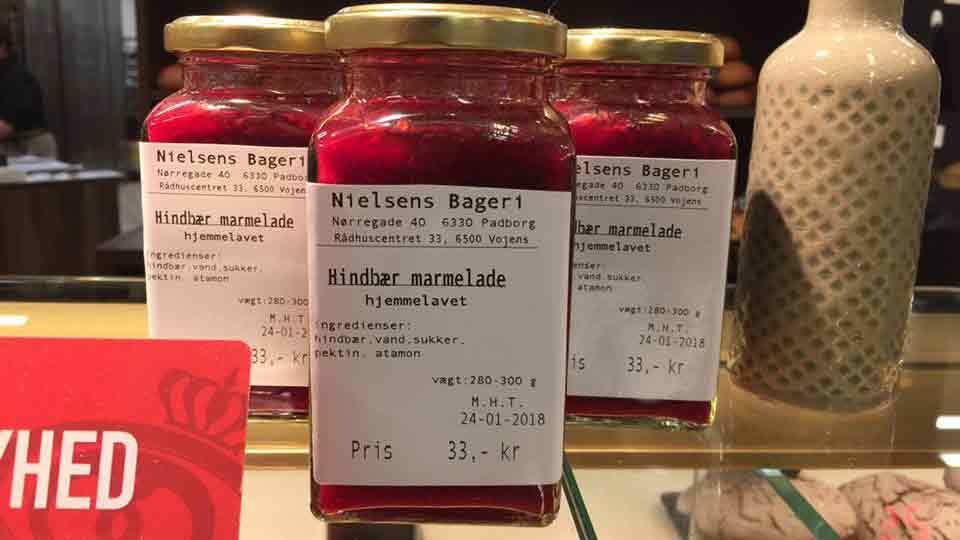Glas med hindbærmarmelade fra Nielsens Bageri, prissat til 33 kr. med etiket og dato.