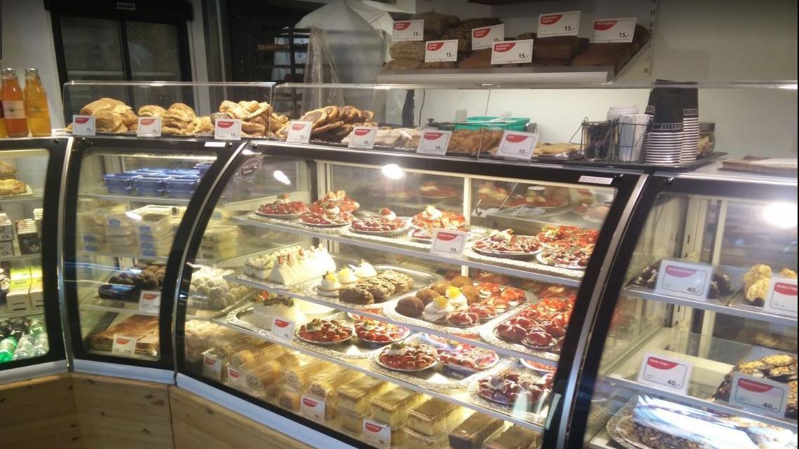 Bageridisplay med forskellige kager, småkager og brød i en bagerbutik. Lys og indbydende atmosfære.