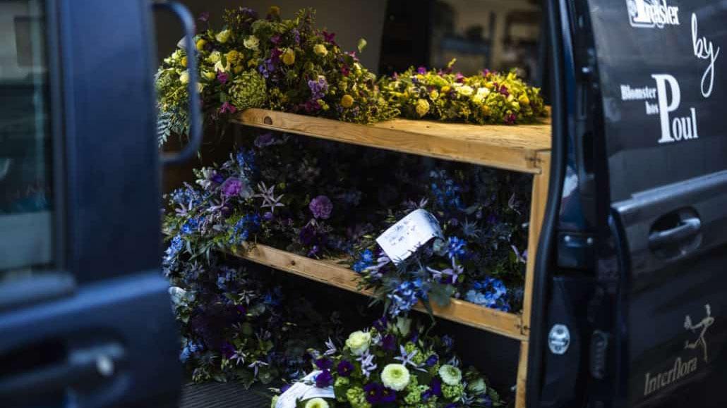 En varevogn med blomsterarrangementer på hylder, herunder lilla og grønne blomster.