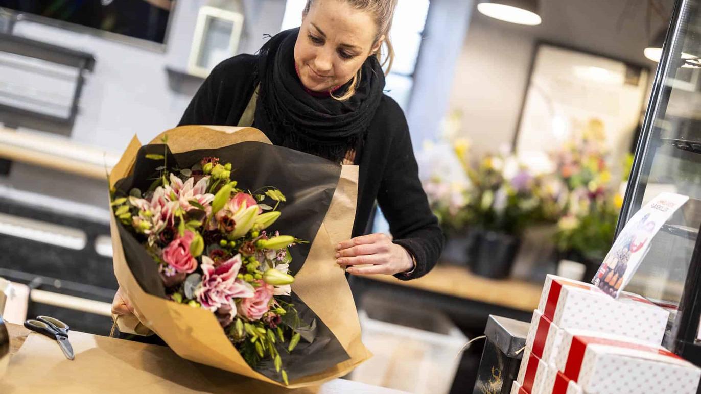 En kvinde pakker en buket blomster ind i brunt papir i en blomsterbutik.
