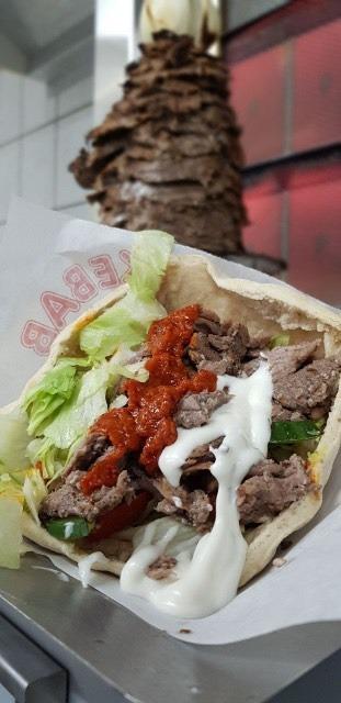 Lækkert kebabwrap med oksekød, salat, tomatsauce og hvidløgssauce, serveret i en tortilla.