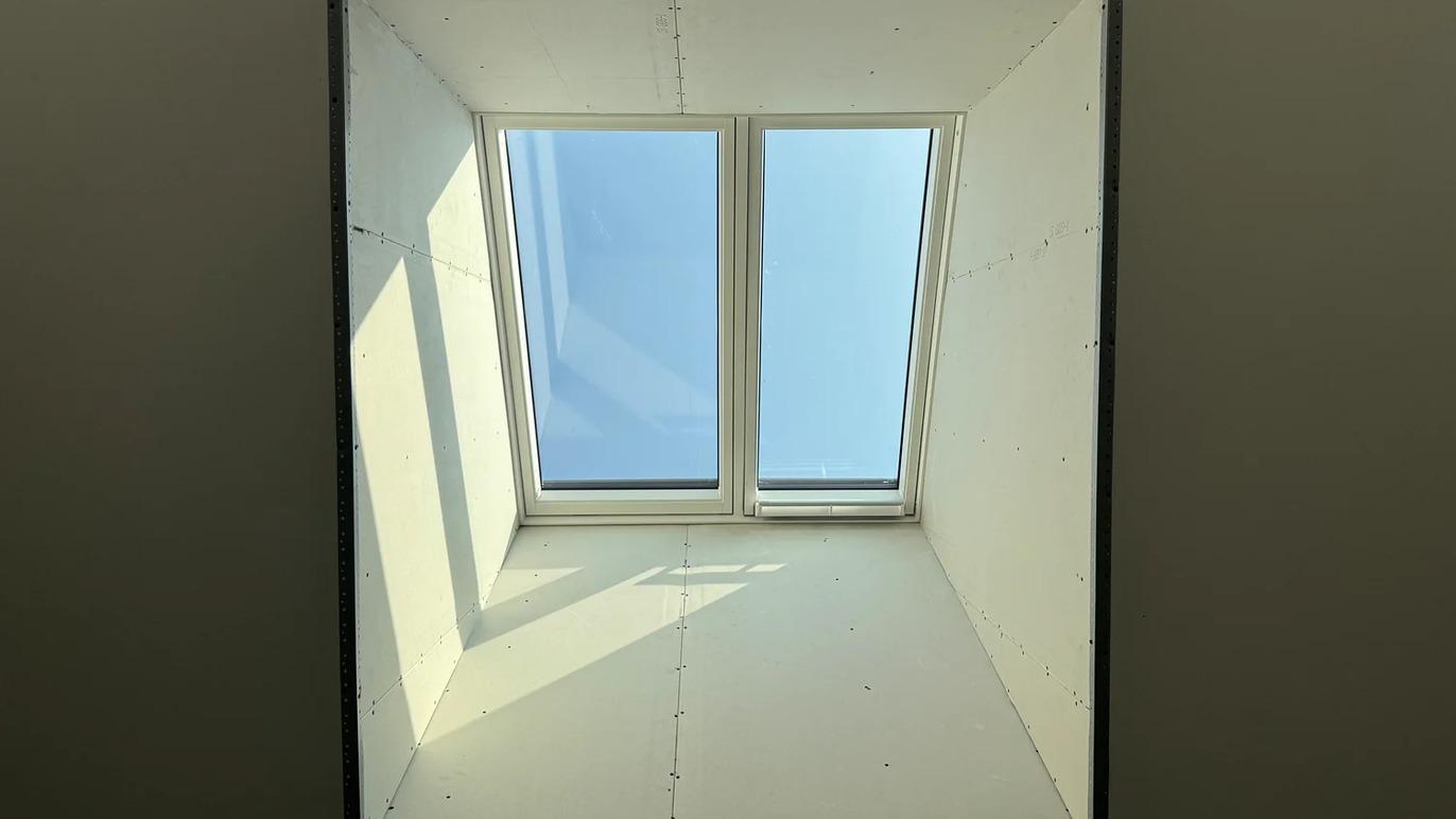 Udsigt opad gennem to vinduer i loftet, der viser en klar blå himmel og sollys.