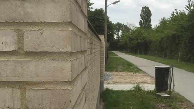 En mur af betonblokke ved en sti med græs og en affaldsspand i nærheden.