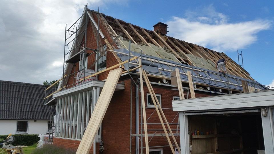 Hus med tagrenovering, stillads og træmaterialer synlige på siden af bygningen under arbejdet.