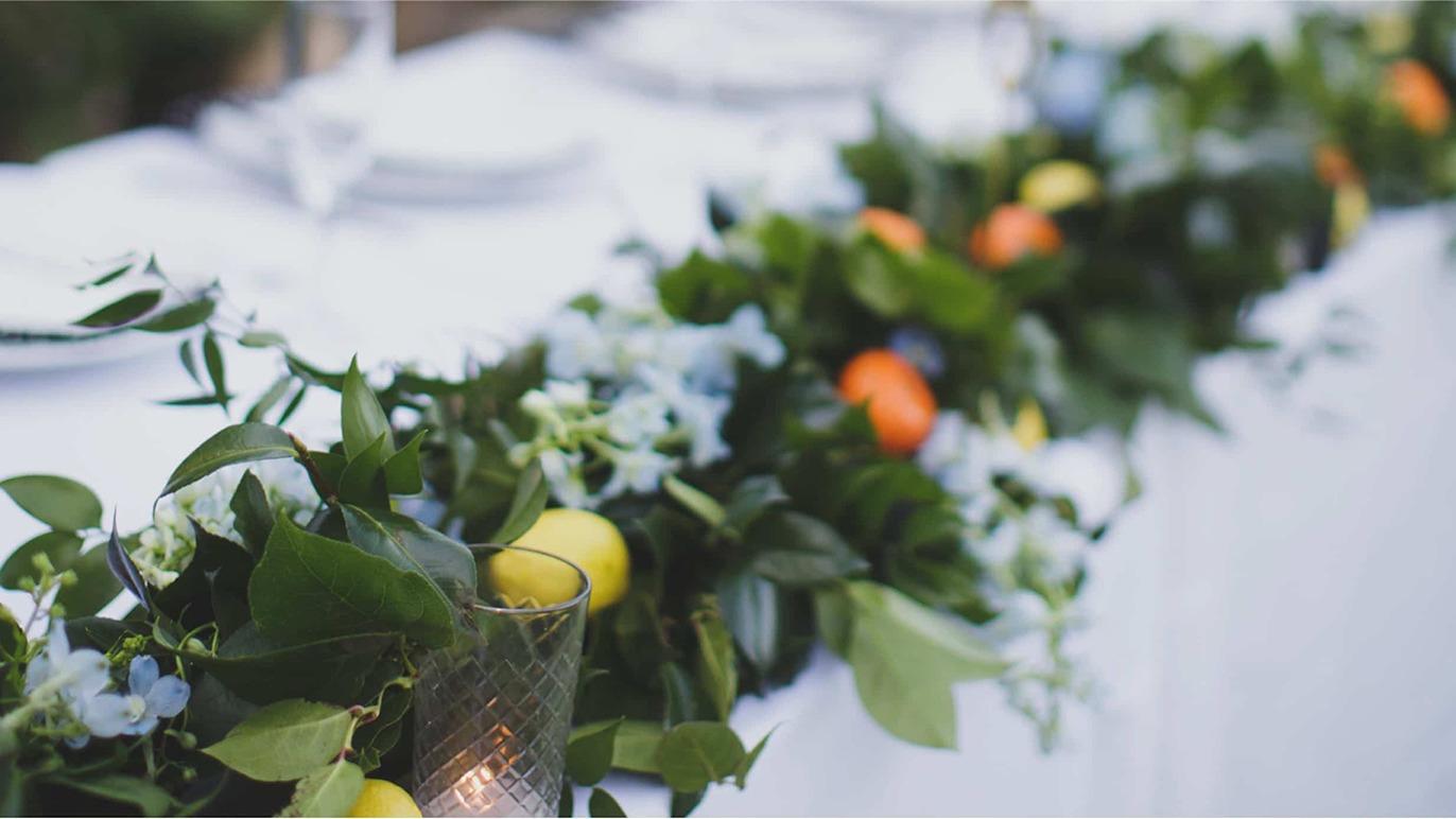 En smuk borddækning med grønne planter, blomster og frugter som citroner og appelsiner.