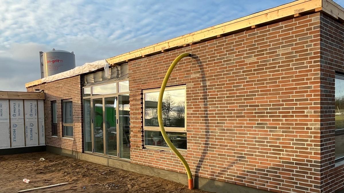 Nybygget murstenshus med store vinduer og en gul slange ved indgangen.