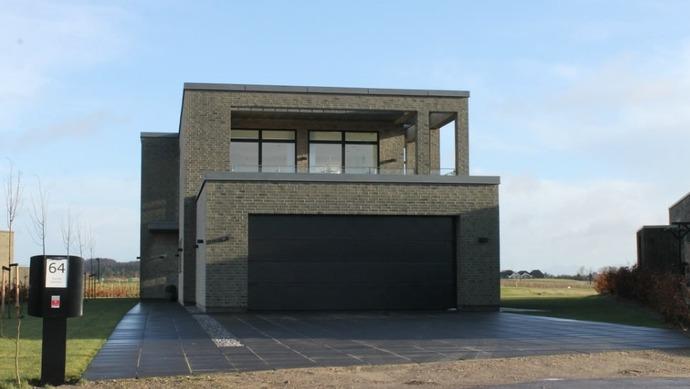 Moderne grå hus med garage og store vinduer beliggende i et åbent landskab.