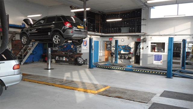 Billede af et autoværksted med en bil på lift og flere værktøjer og udstyr i baggrunden.