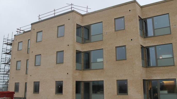 Nyt byggeri af en moderne murstensbygning med store vinduer og altaner. Scaffolding er synligt i baggrunden.