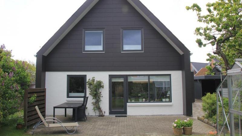 Moderne hus med sort facade, store vinduer og en terrasse med havemøbler i haven.