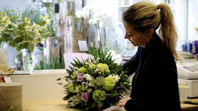 Blomsterhandler, der arrangerer en buket med farverige blomster i en blomsterbutik.