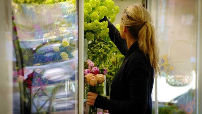 En kvinde vælger blomster i en blomsterbutik med farverige buketter i baggrunden.