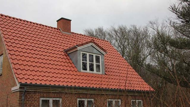 Et hus med rødt tag og vinduer, omgivet af træer under en grå himmel.