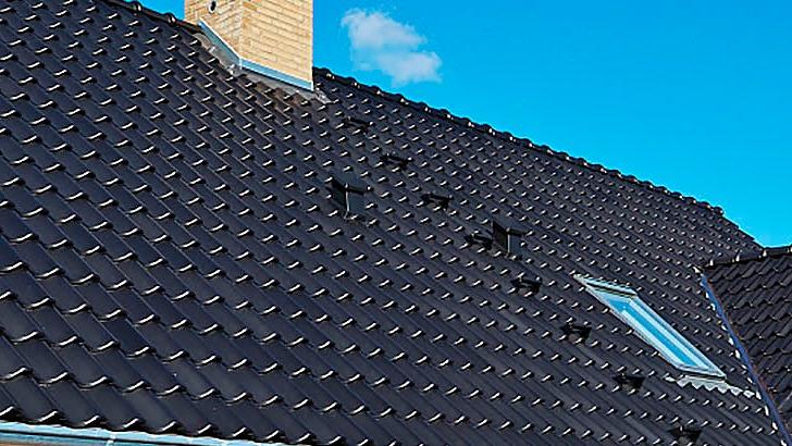 Tag med sorte teglsten og en skorsten under en blå himmel.