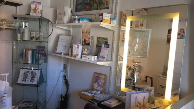 Et skønhedssalon med hylder fyldt med produkter, en spejl med lys og en behagelig atmosfære.