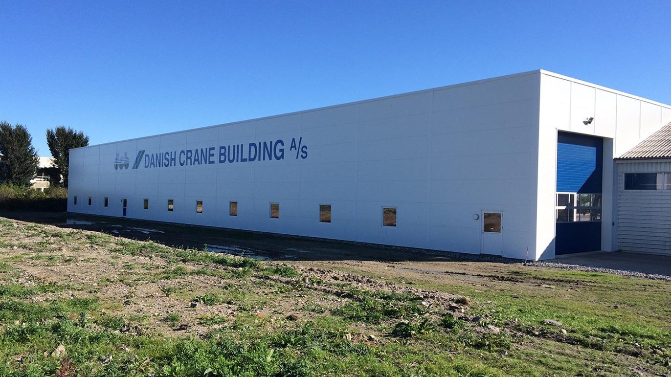 Moderne bygning med hvid facade og store vinduer, beliggende på en græsmark under en klar blå himmel.