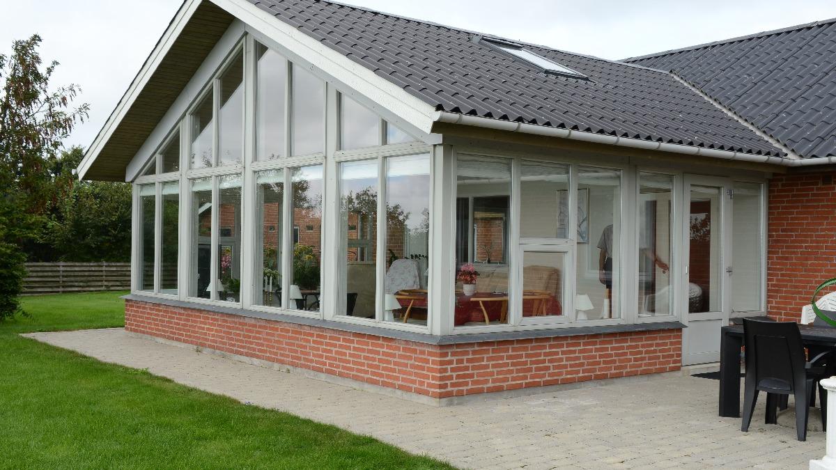 En moderne murstensvilla med store vinduer og en glasoverdækket terrasse i haven.