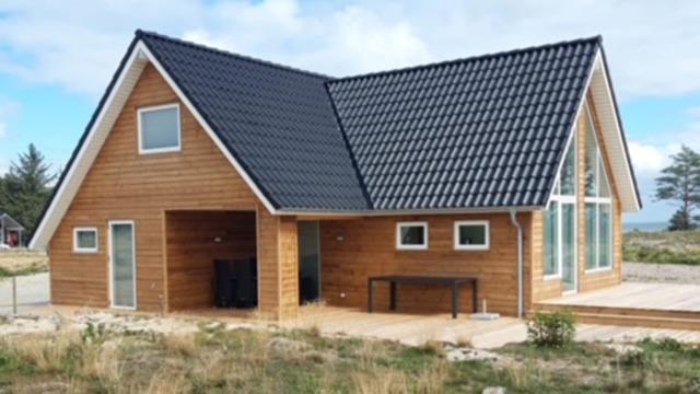 Moderne træhus med sort tag og store vinduer, beliggende i et naturskønt område.