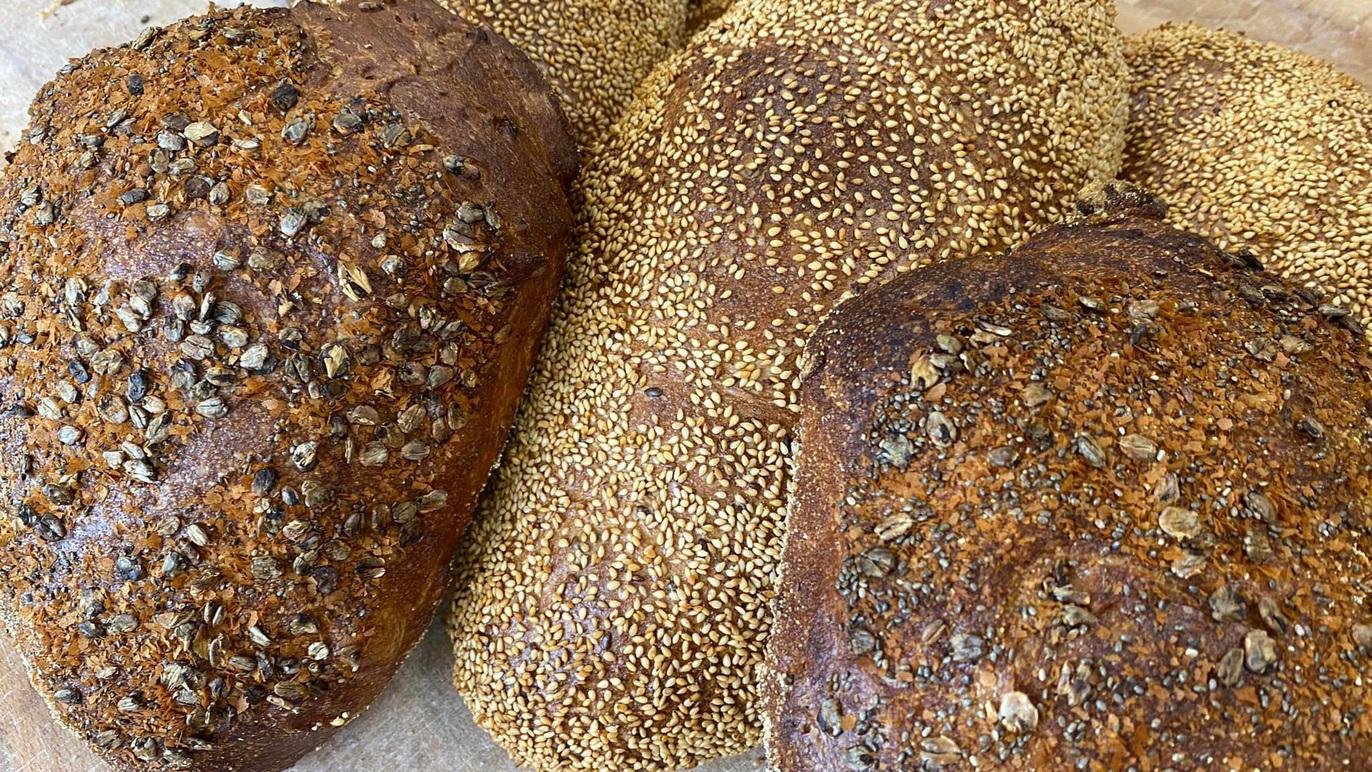 Friskbagt brød med sesamfrø og frø på overfladen, præsenteret på en bageplade.
