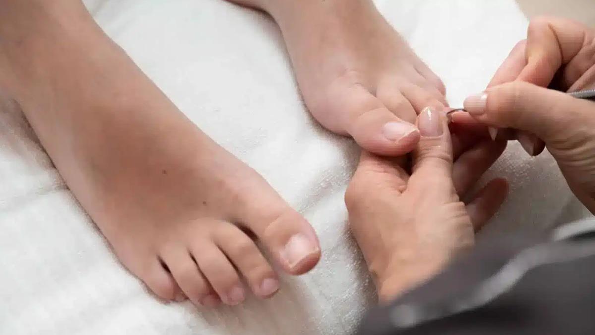 En person får pedicure, mens en anden person plejer tåneglene på en hvid håndklæde.