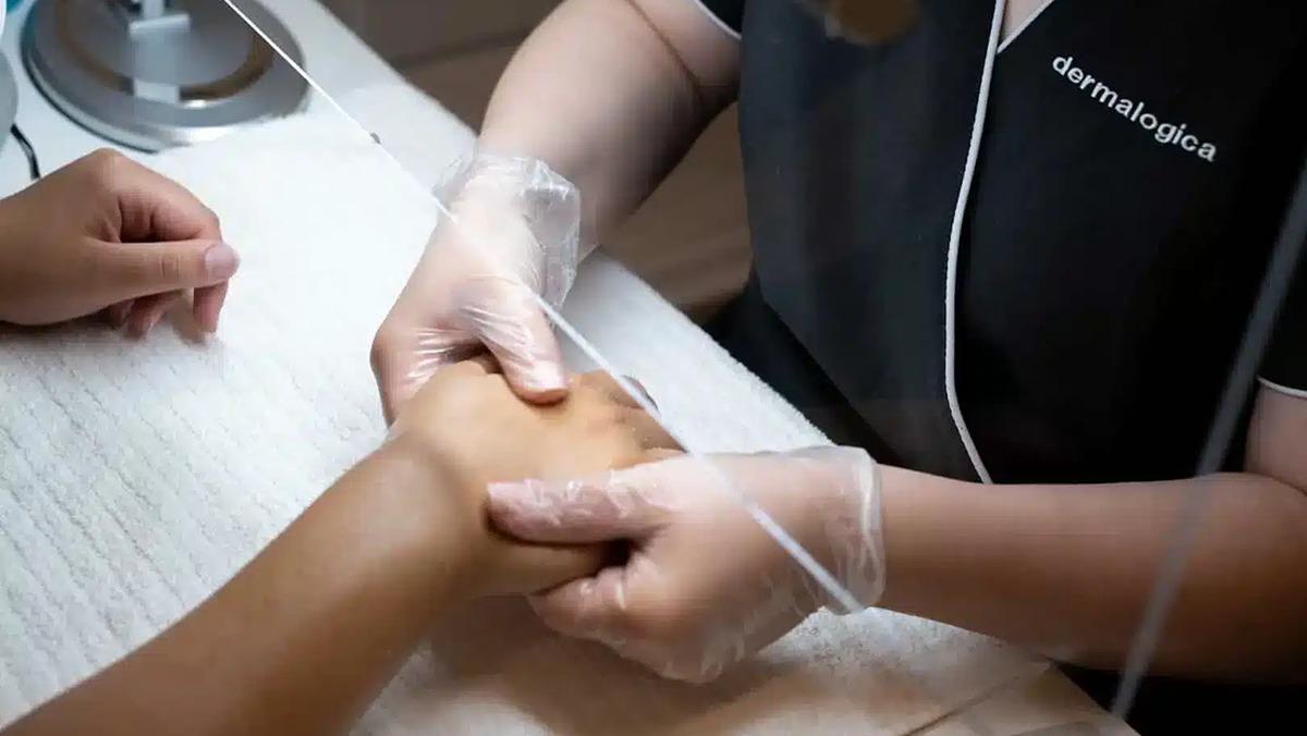 Håndbehandling med hudplejeprodukter i en skønhedssalon, hvor en behandler masserer en klients hånd.