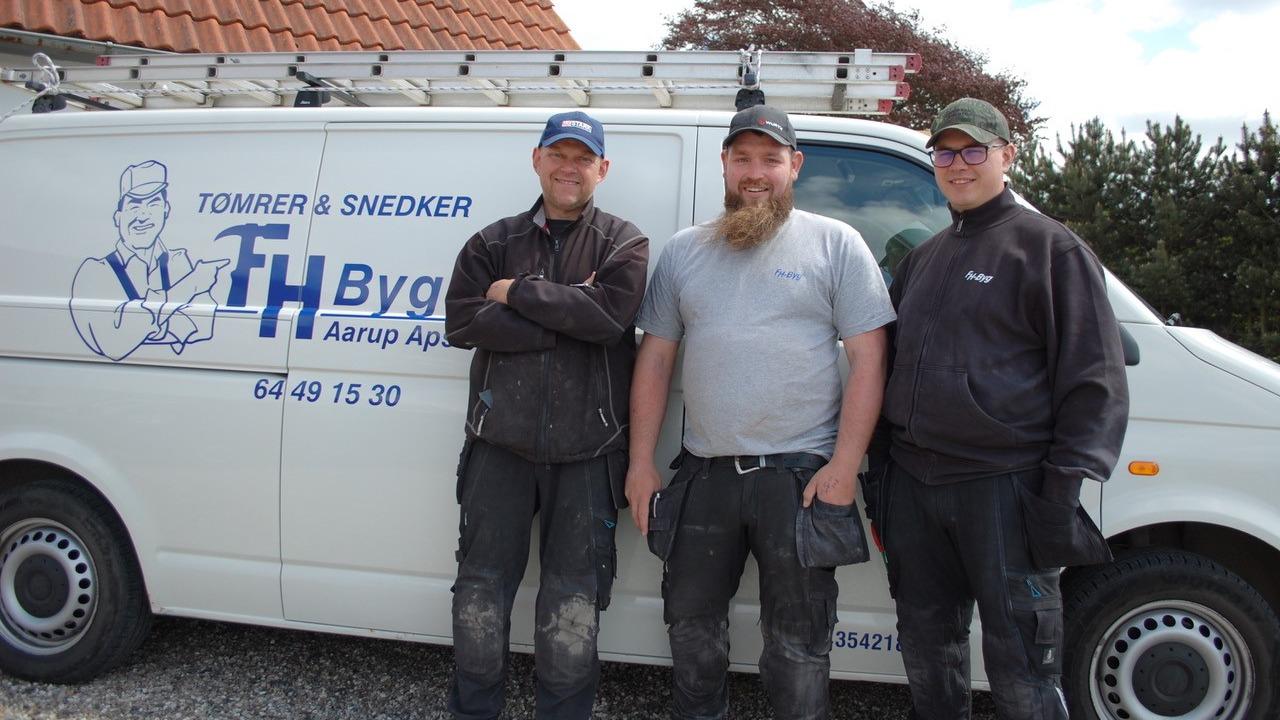 Tre håndværkere står foran en hvid varevogn med logoet fra TH Byg. De ser glade og afslappede ud.