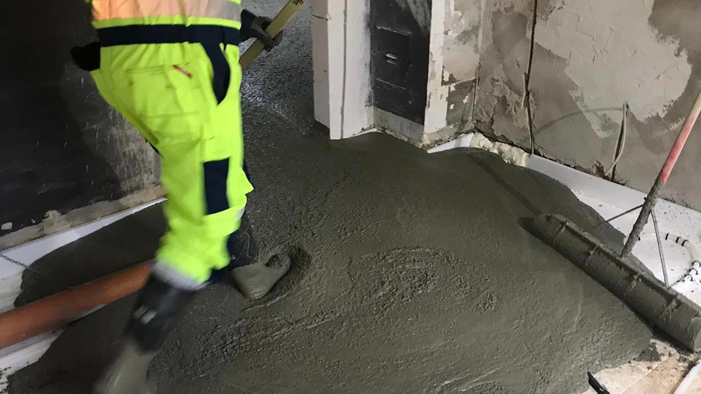 En arbejdstager i sikkerhedstøj hælder beton på gulvet i et renoveringsprojekt.