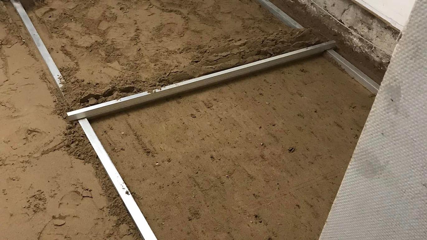Billede af en sandet gulvbelægning med metalramme, der er klar til at blive jævnet ud i et rum.