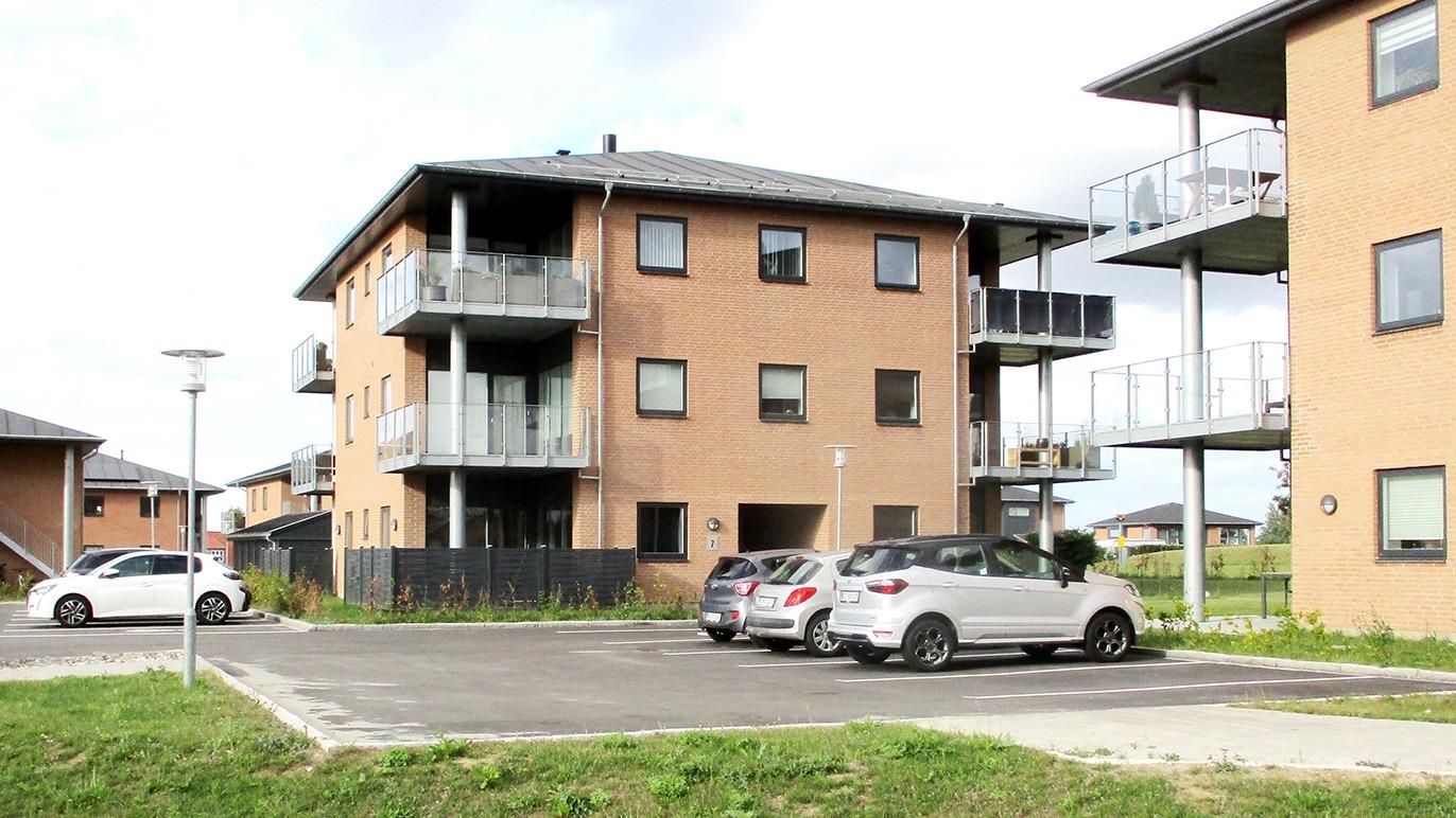Moderne lejlighedskompleks med parkeringsplads og biler foran bygningen.