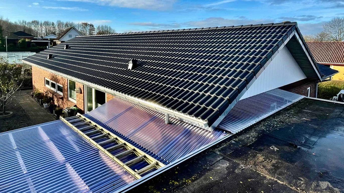 Tag med solceller på et hus, der har en udestue og en klar blå himmel i baggrunden.