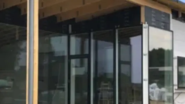 Moderne bygning med store glasvægge og trædetaljer, der viser en del af konstruktionen.