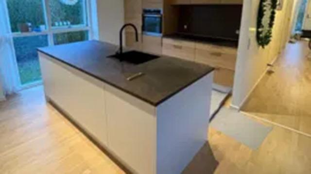 Moderne køkken med en stor ø, sort bordplade og minimalistisk indretning i lyse farver.