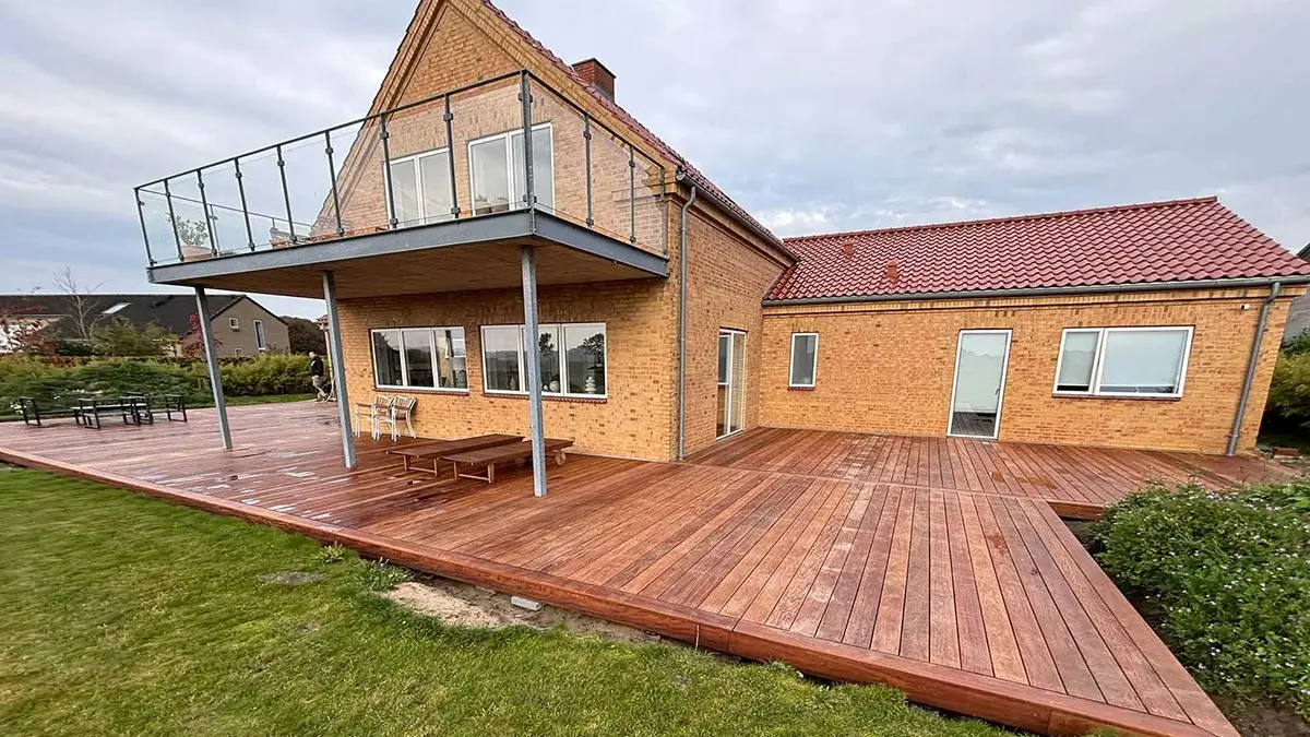 En moderne murstensvilla med en stor træterrasse og balkon, beliggende i et roligt område.