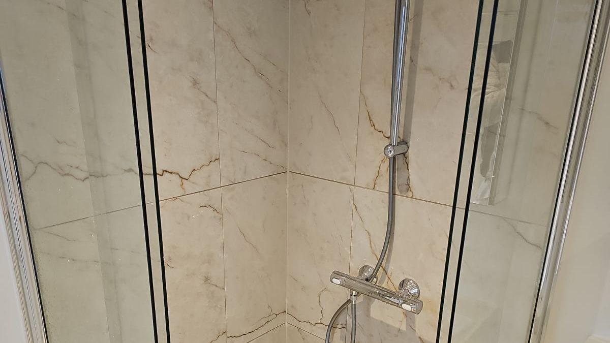 Brusekabine med glasvægge og moderne bruser, indrettet med marmorlook og kromdetaljer.