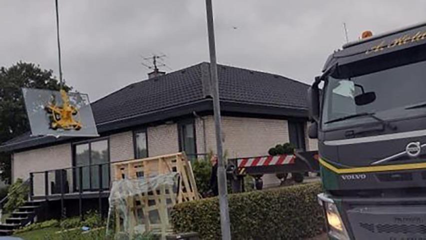 Lastbil løfter tagplader ved et hus under renovering, med grå himmel i baggrunden.