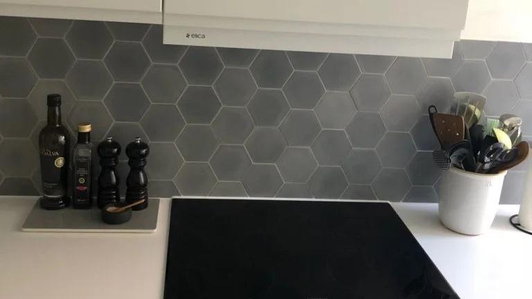 Køkkenbord med sort kogeplade, hexagonfliser og krydderikværne i sort og hvid.